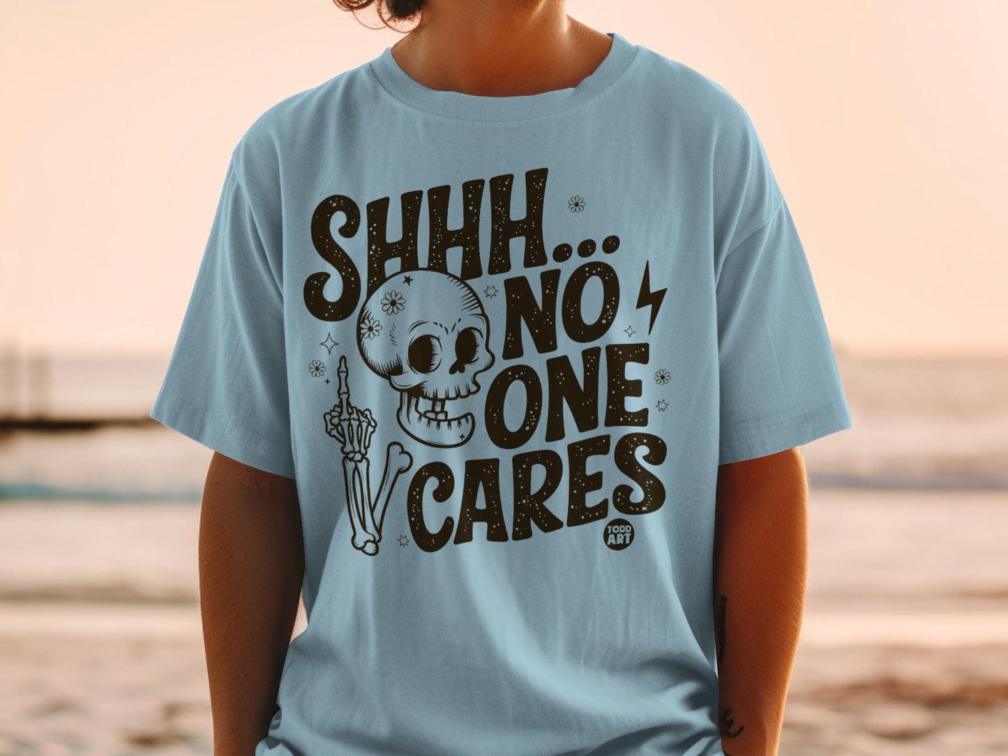 Light blue t-shirt with "SHHH... NO ONE CARES" text and skull graphic.