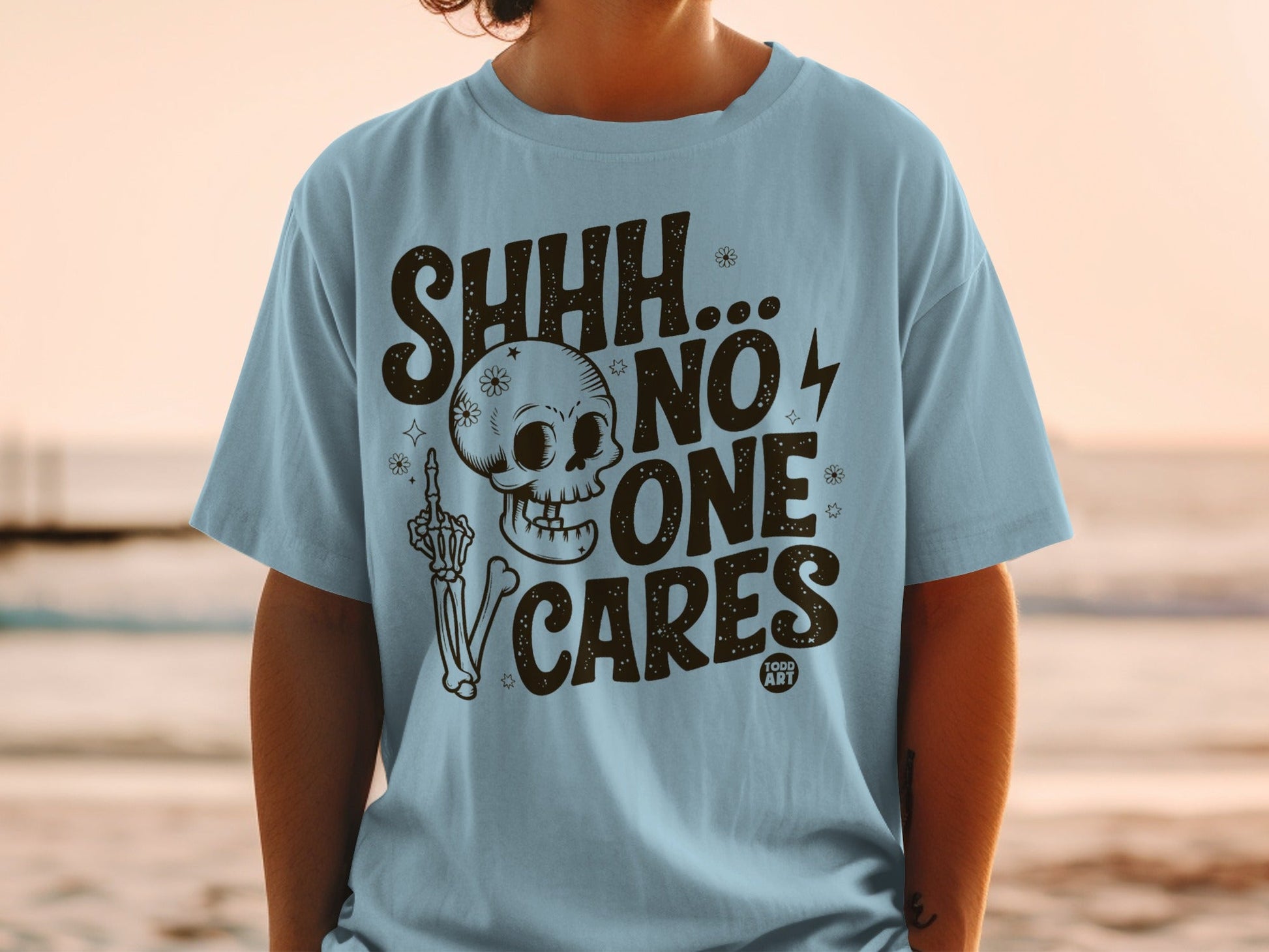 Light blue t-shirt with "SHHH... NO ONE CARES" text and skull graphic.