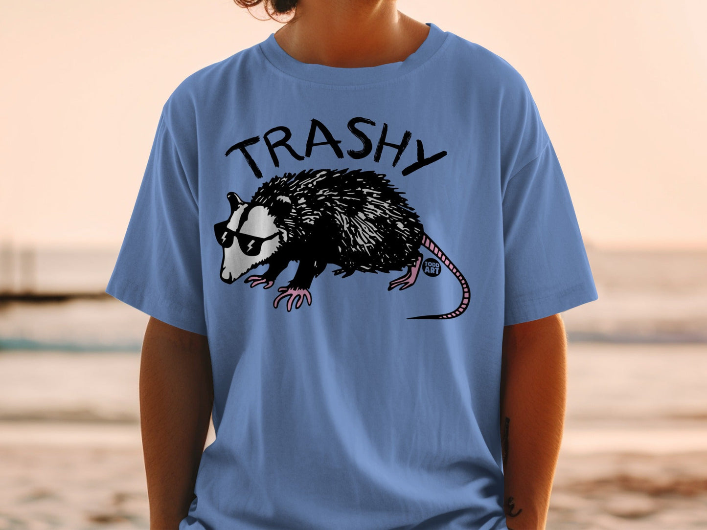 Blue t-shirt with a cartoon opossum wearing sunglasses and "TRASHY" text.
