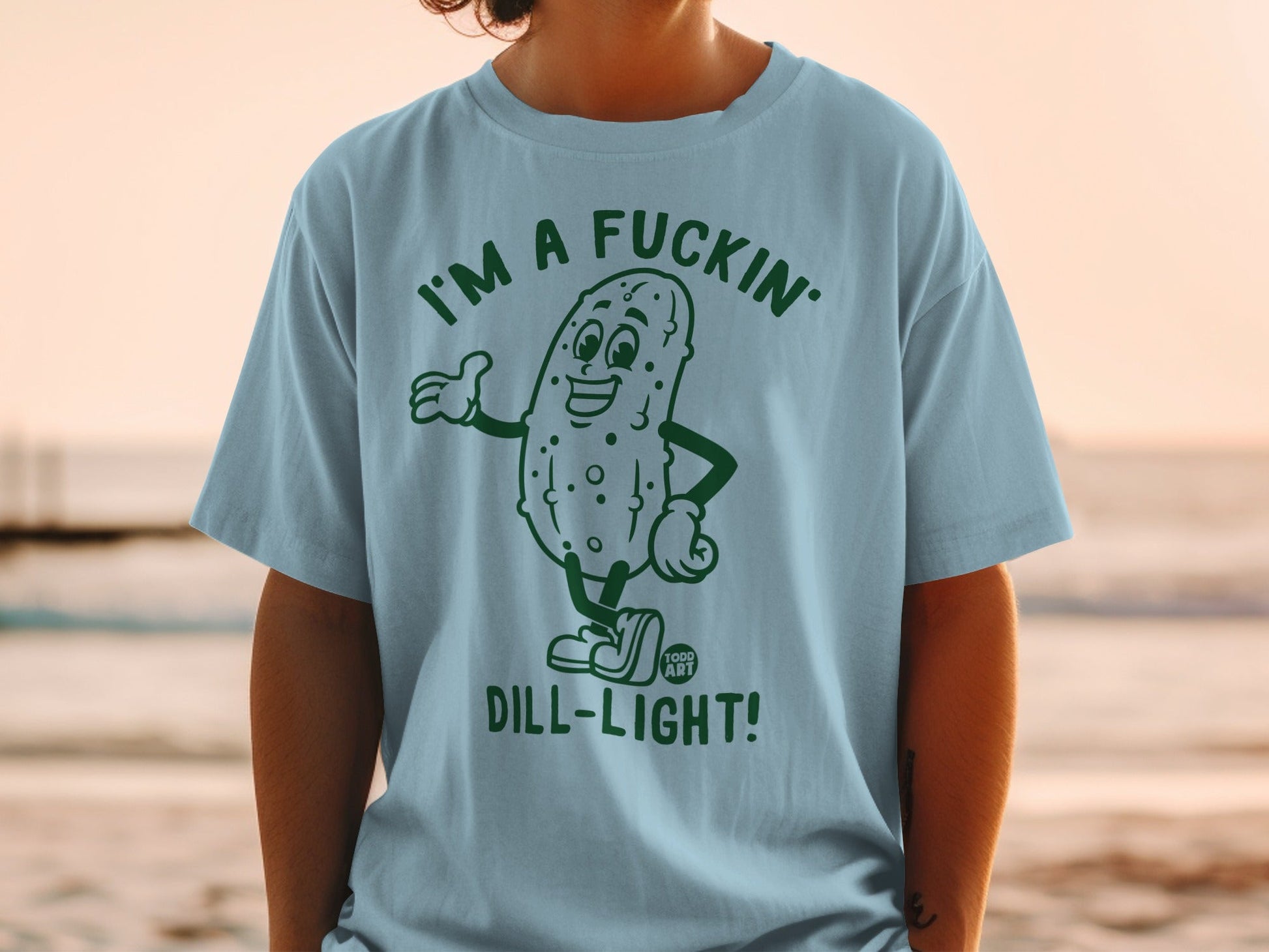 Light blue t-shirt with a cartoon pickle wearing sunglasses, proclaiming "I'M A FUCKIN' DILL-LIGHT!".