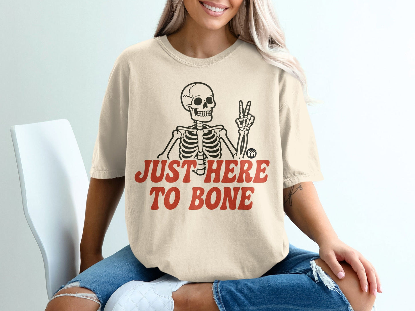 T-shirt with skeleton giving peace sign, "JUST HERE TO BONE" text.