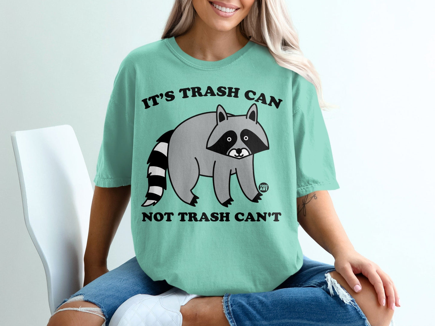 Teal t-shirt with raccoon graphic and text "IT'S TRASH CAN NOT TRASH CAN'T".