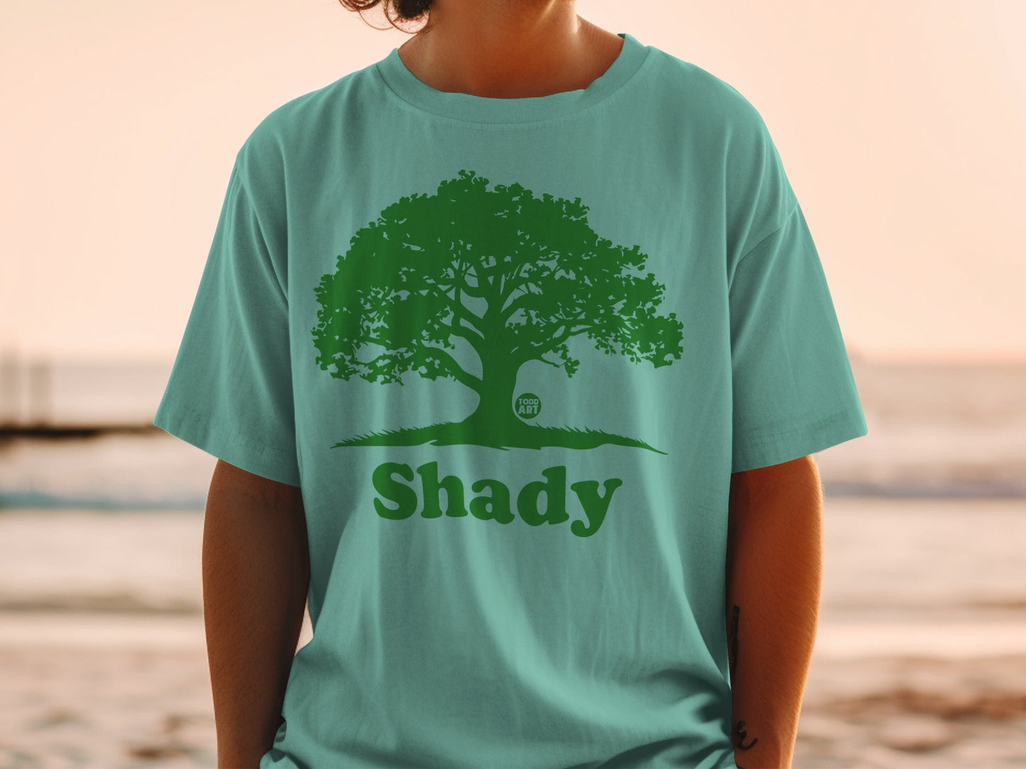 Green tree logo with "Shady" text on a teal t-shirt.