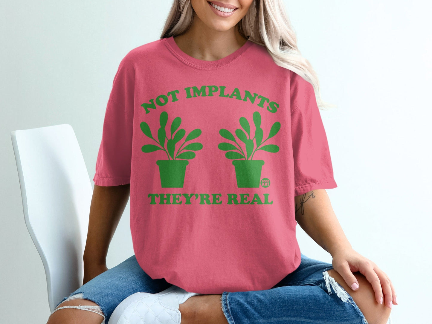 Pink t-shirt with green text and plant graphics: "NOT IMPLANTS THEY'RE REAL".