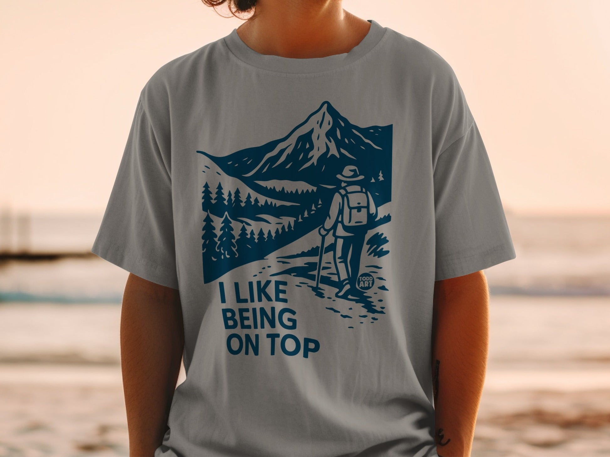 Grey t-shirt with blue mountain, trees, and hiker graphic and text "I LIKE BEING ON TOP".