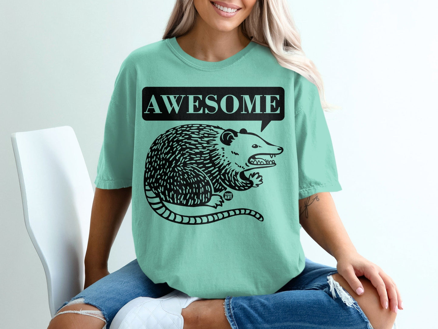 Teal t-shirt with black opossum graphic and "AWESOME" speech bubble.