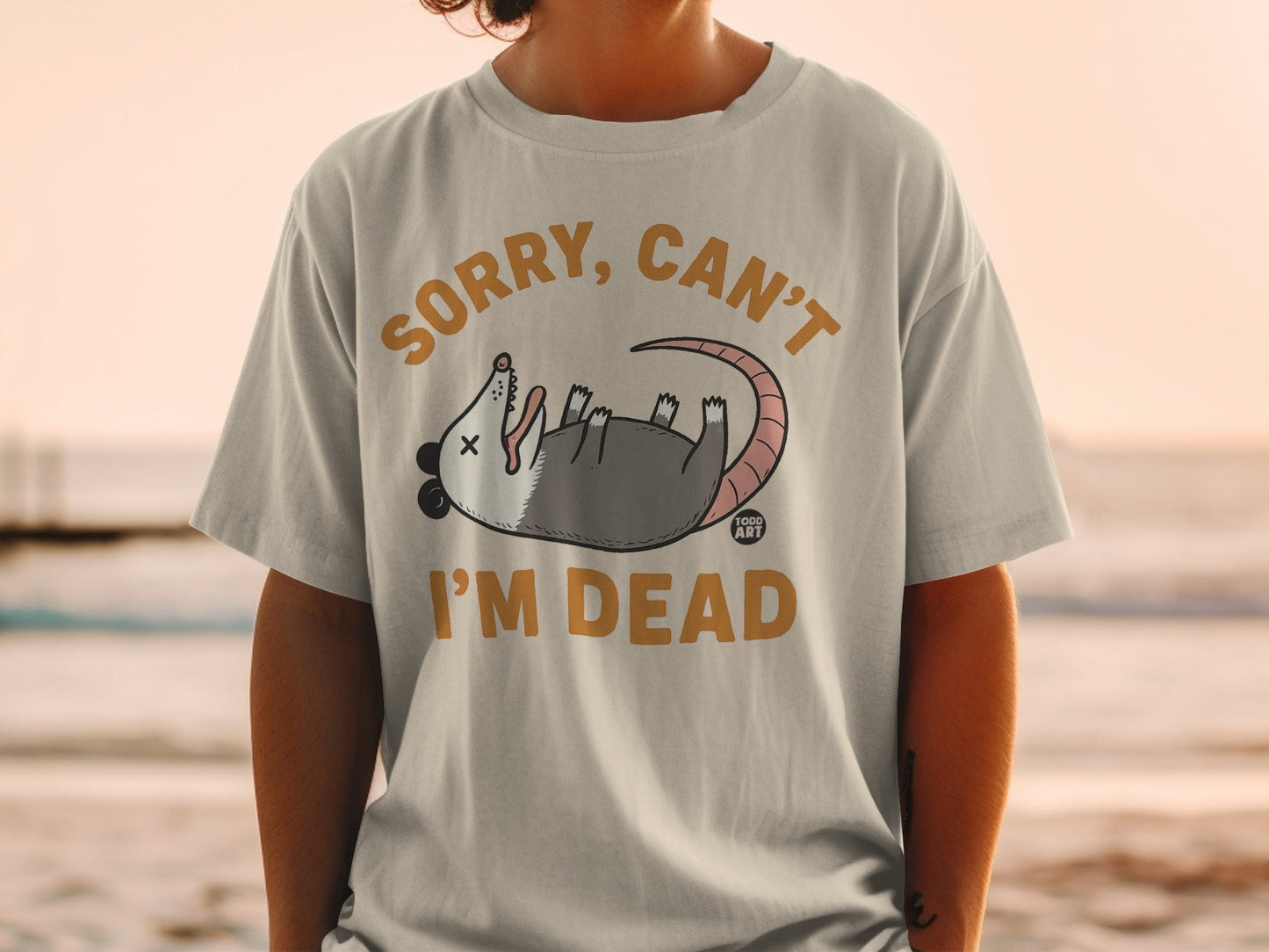 T-shirt with cartoon opossum playing dead, text "SORRY, CAN'T I'M DEAD."
