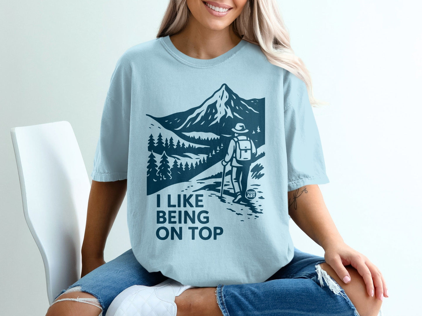 Light blue t-shirt with mountain and hiker graphic, text "I LIKE BEING ON TOP".