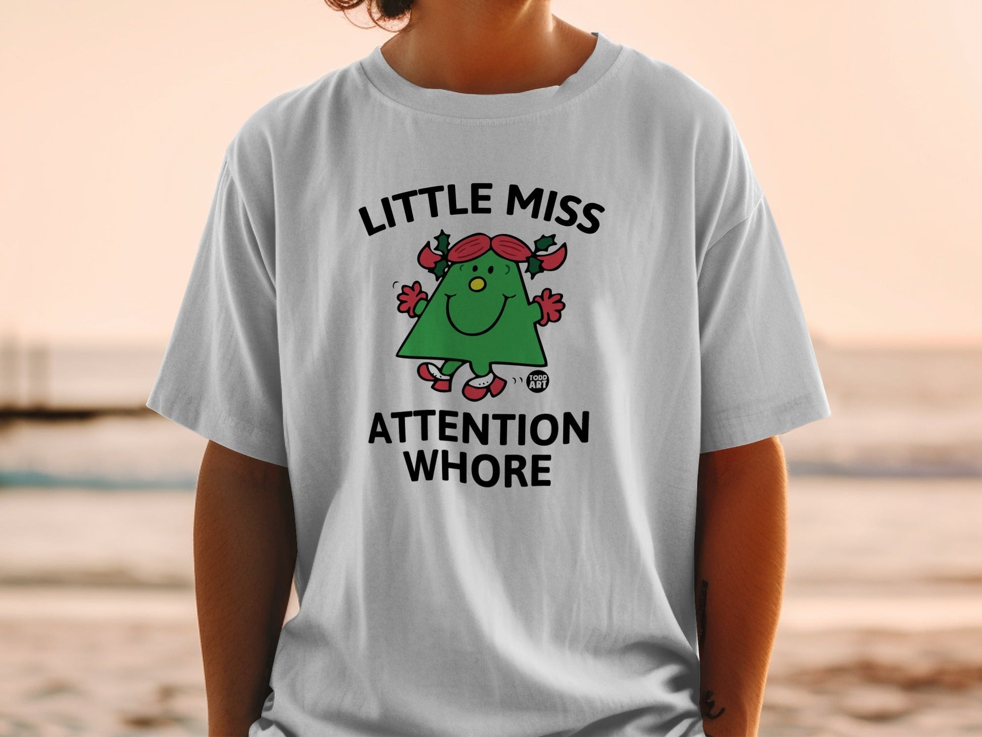 White t-shirt with "Little Miss Attention Whore" graphic of a Christmas tree character.