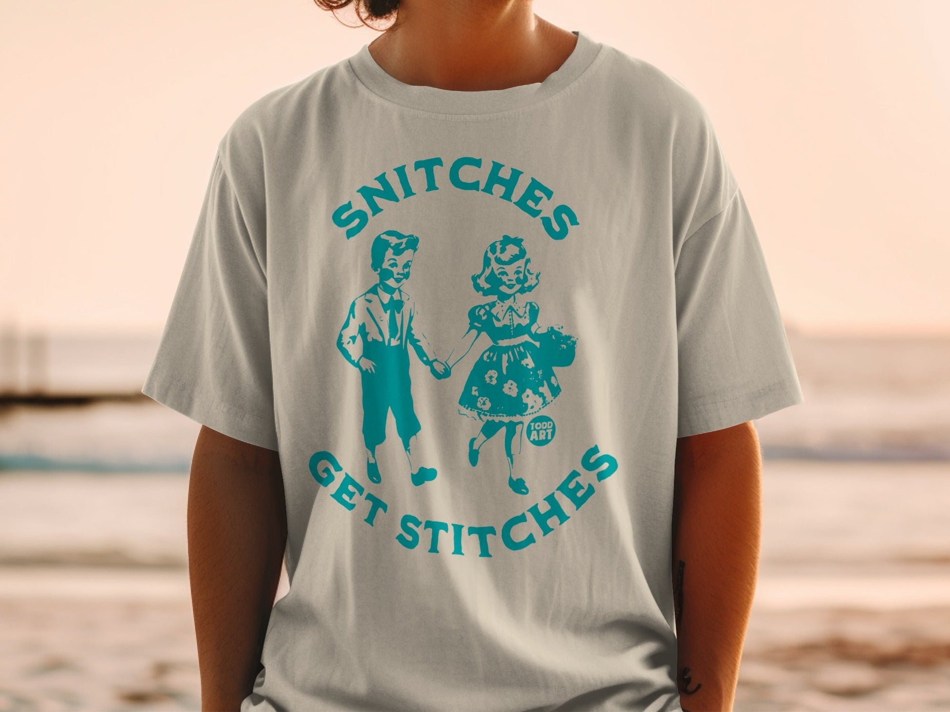 Blue graphic on a light blue t-shirt of two children holding hands, "Snitches Get Stitches".