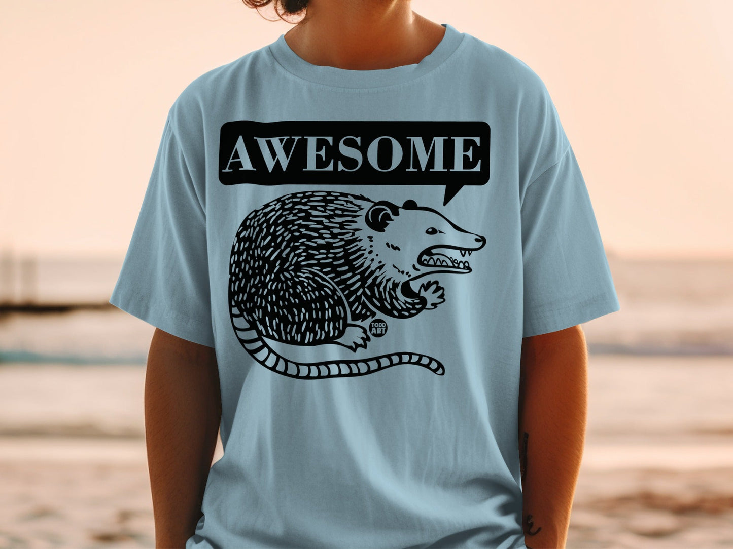 Light blue t-shirt with a black cartoon opossum and "AWESOME" speech bubble.