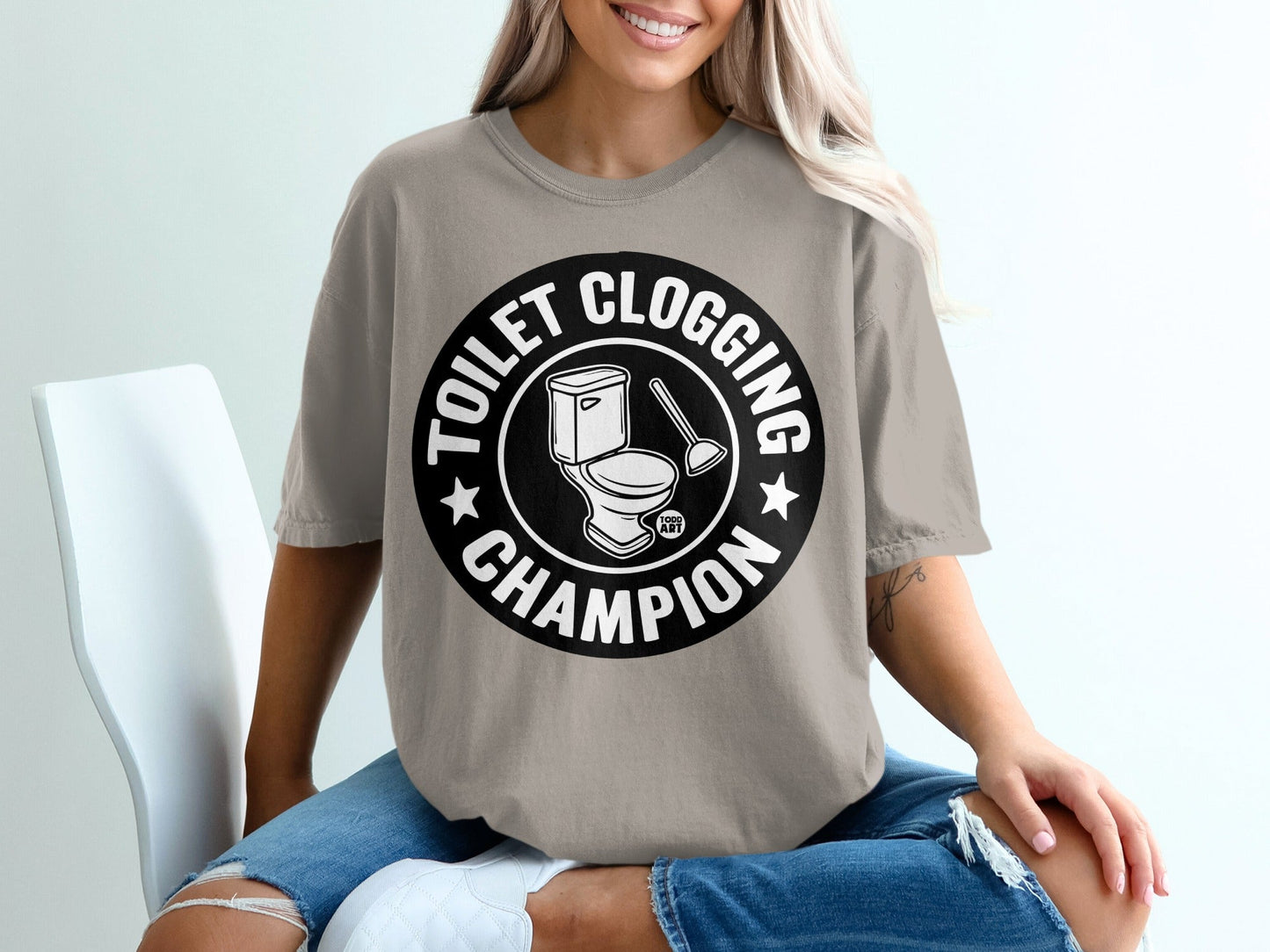 Toilet clogging champion graphic on a t-shirt with toilet and plunger illustration.