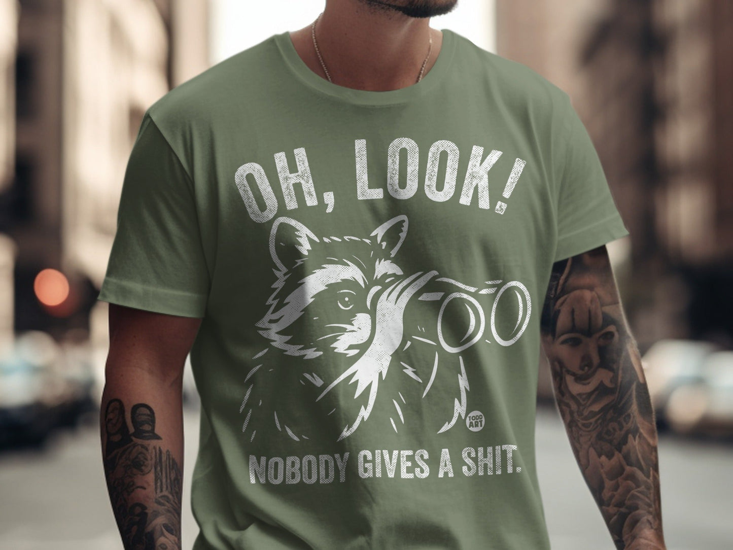 Green t-shirt with white graphic of a raccoon holding binoculars and the text "OH, LOOK! NOBODY GIVES A SHIT."