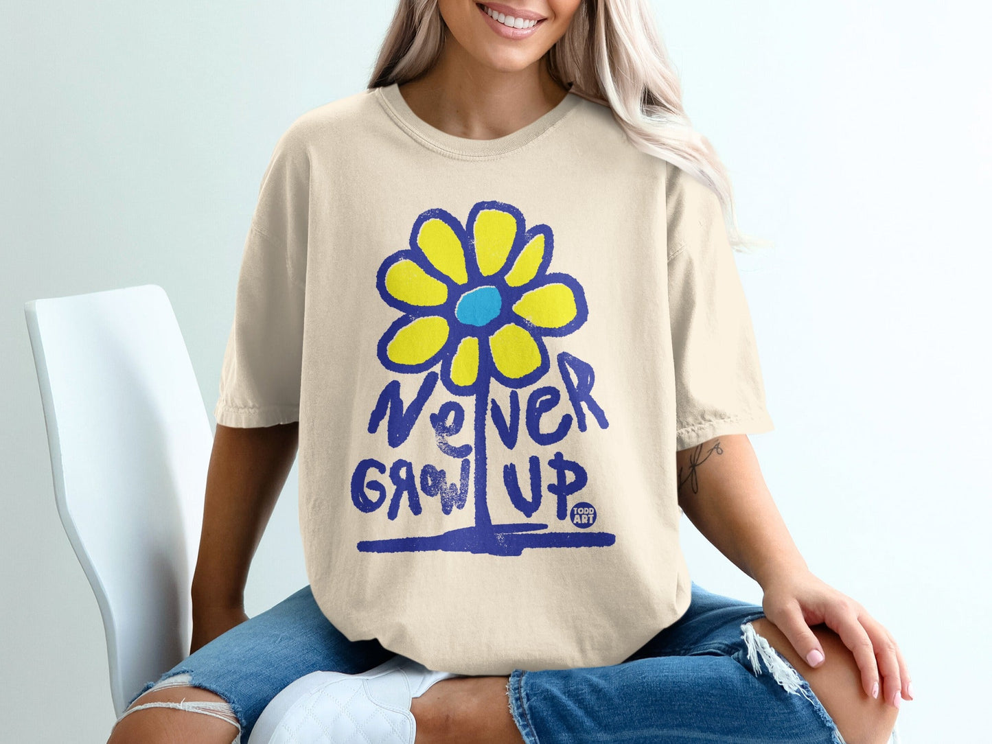 Cream t-shirt with yellow and blue flower graphic and "Never Grow Up" text.