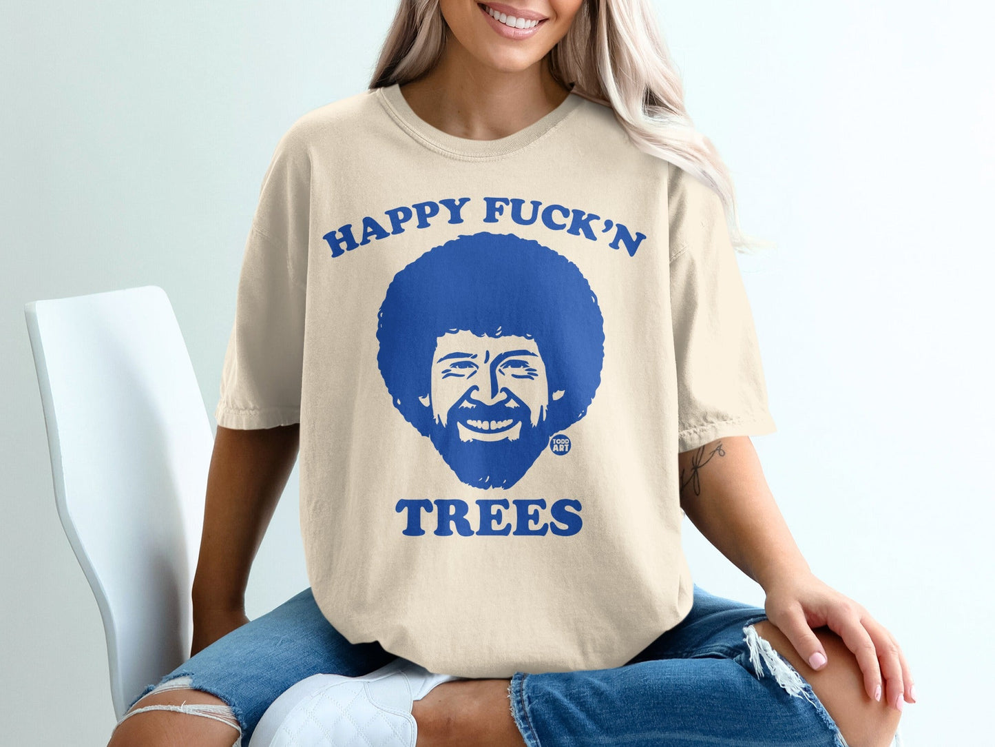Bob Ross graphic tee with text "Happy Fuck'n Trees" on cream t-shirt.