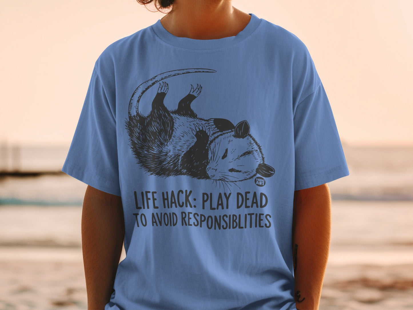Blue t-shirt with opossum design and "LIFE HACK: PLAY DEAD TO AVOID RESPONSIBILITIES" text.