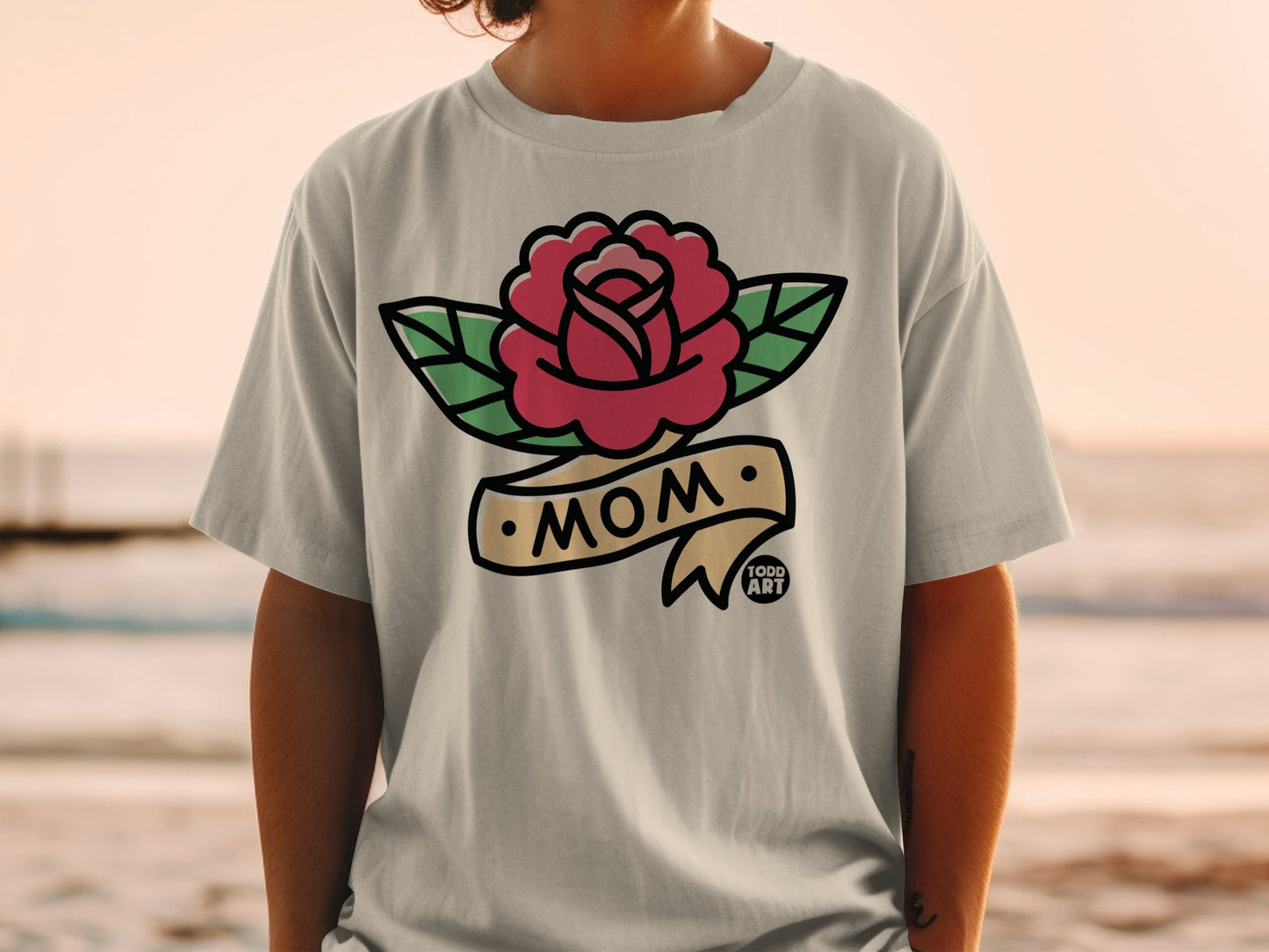 T-shirt with a rose and banner that says "MOM", on a person.