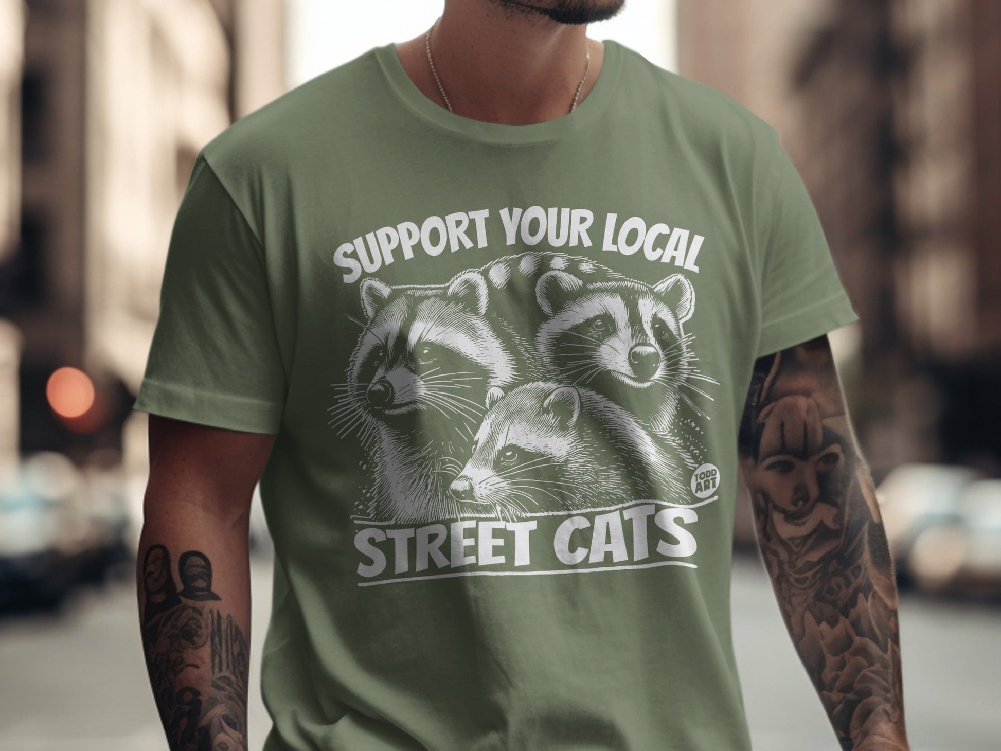 Green t-shirt with raccoons and text "SUPPORT YOUR LOCAL STREET CATS".