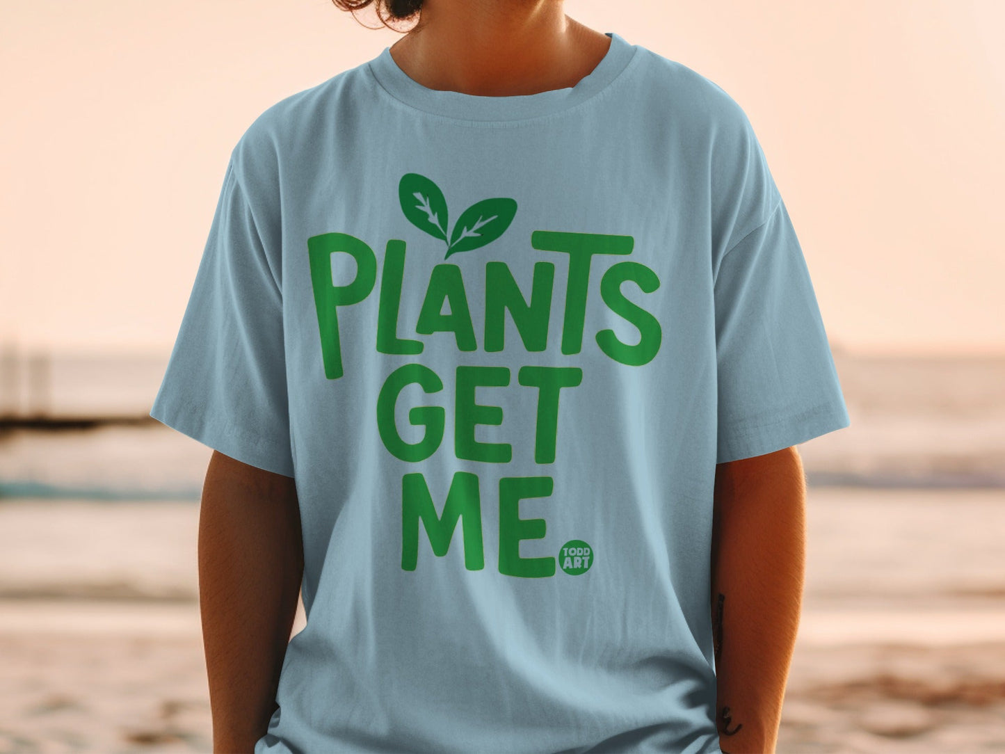 Light blue t-shirt with "PLANTS GET ME" in green text and a small leaf logo.