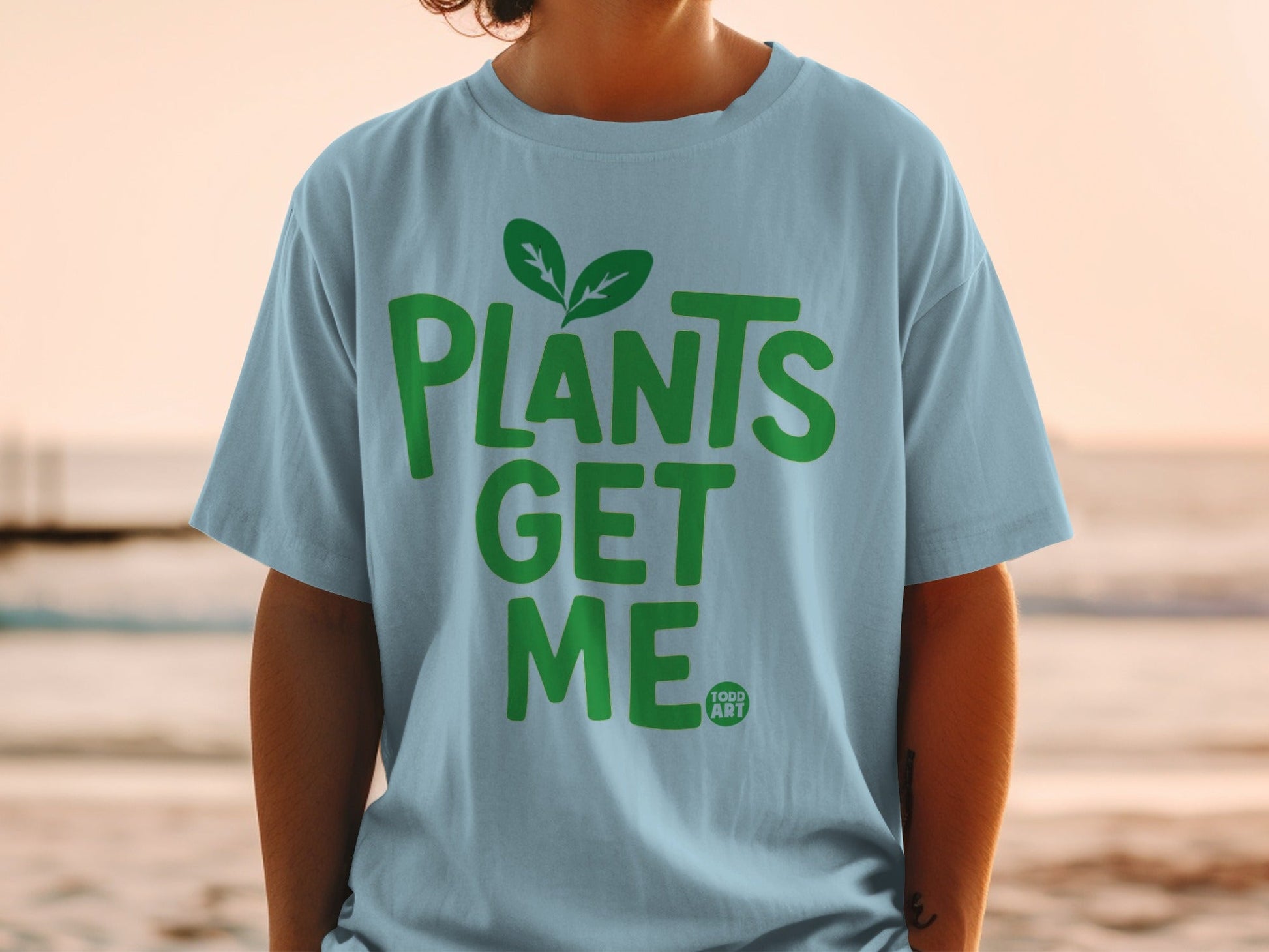 Light blue t-shirt with "PLANTS GET ME" in green text and a small leaf logo.