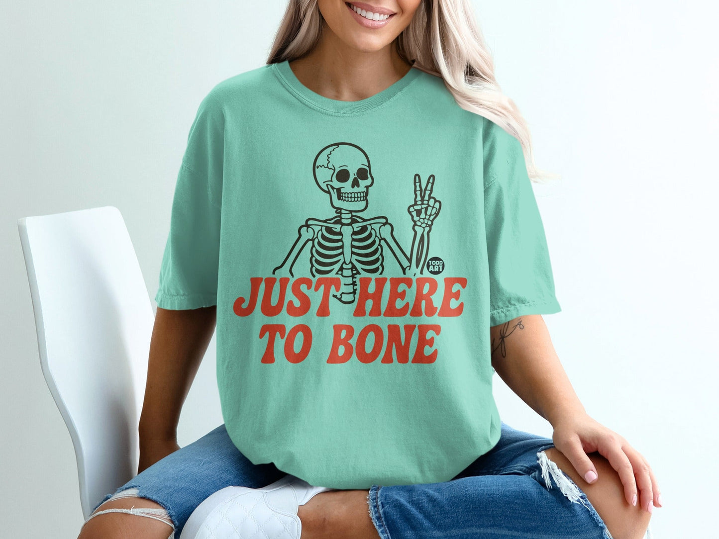 Mint green t-shirt with skeleton giving peace sign and text "JUST HERE TO BONE".