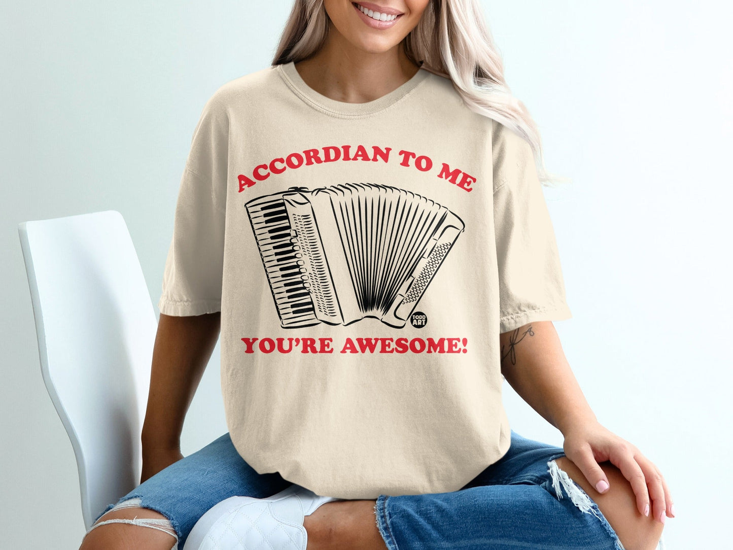 Beige t-shirt with accordion graphic and text "ACCORDION TO ME YOU'RE AWESOME!".