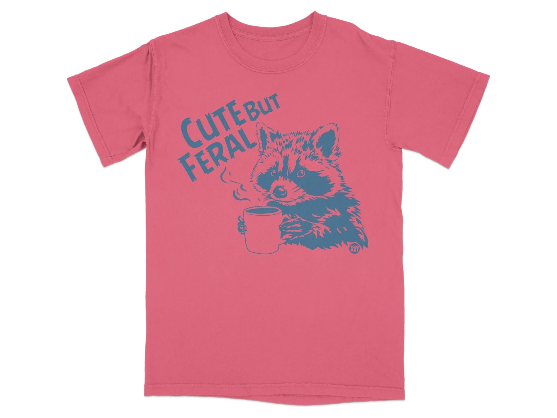 Pink t-shirt with a blue raccoon holding a steaming mug, text reads "CUTE BUT FERAL".