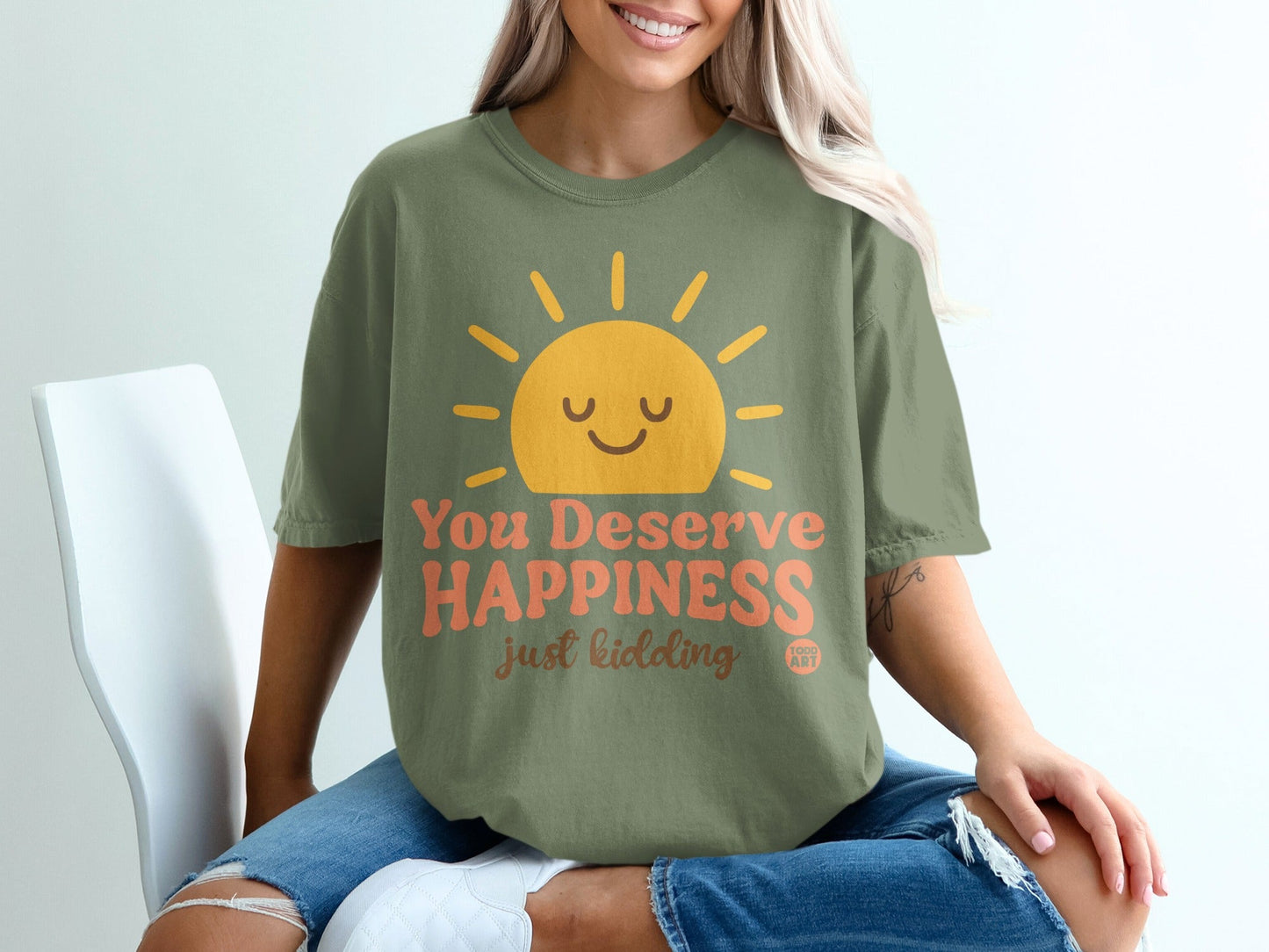 Olive green t-shirt with smiling sun and "You Deserve Happiness just kidding" text.