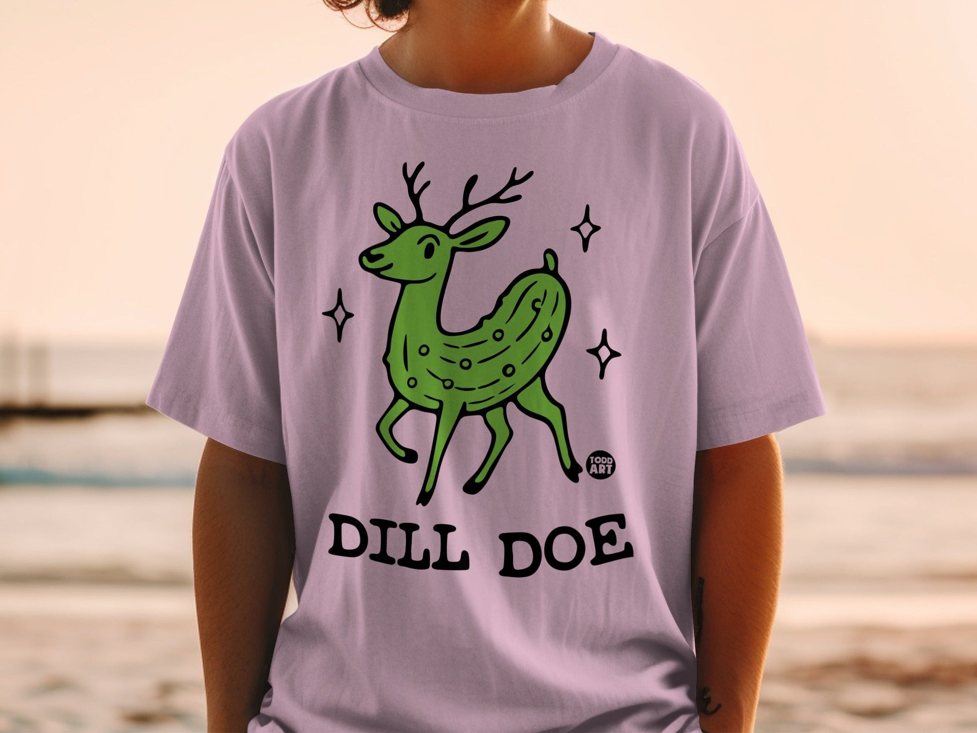 Green pickle deer with antlers on a lilac t-shirt, "Dill Doe" text.