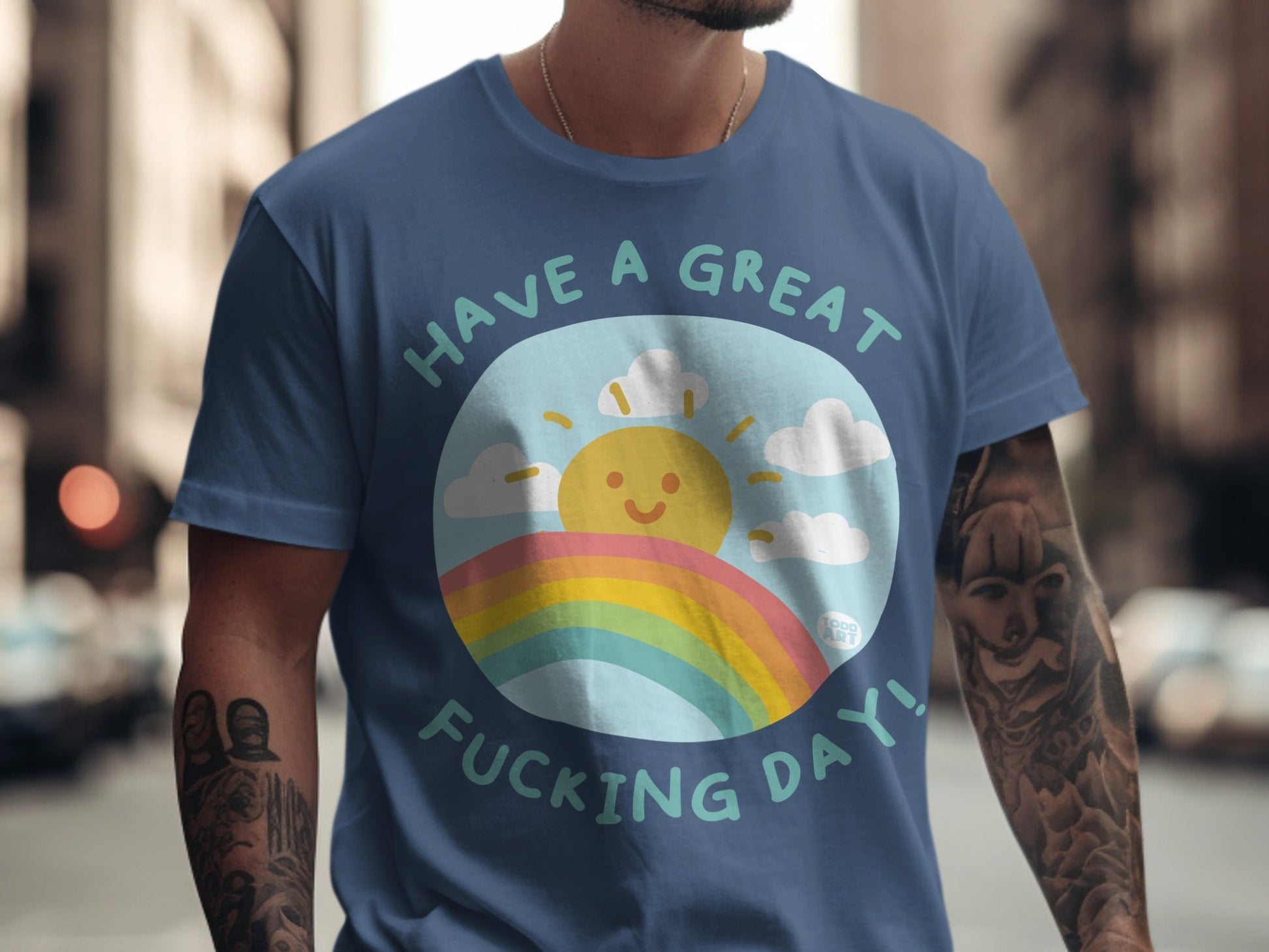 Blue t-shirt with smiling sun, rainbow, and text "Have a great fucking day!".