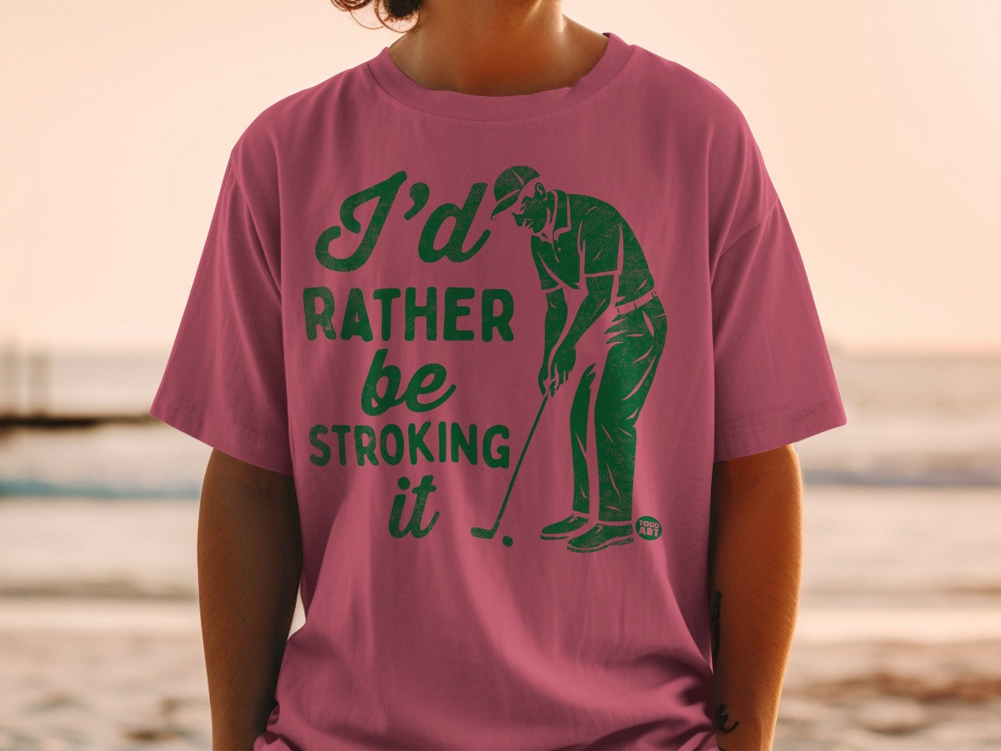 Pink t-shirt with "I'd rather be stroking it" text and golfer graphic.