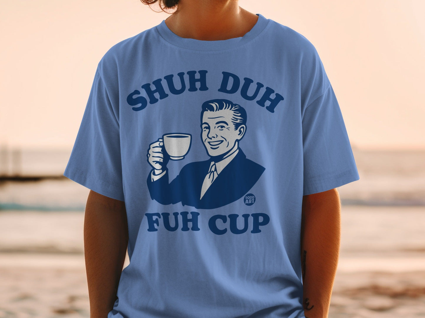 Blue t-shirt with graphic of man holding "Shuh Duh Fuh Cup" coffee mug.