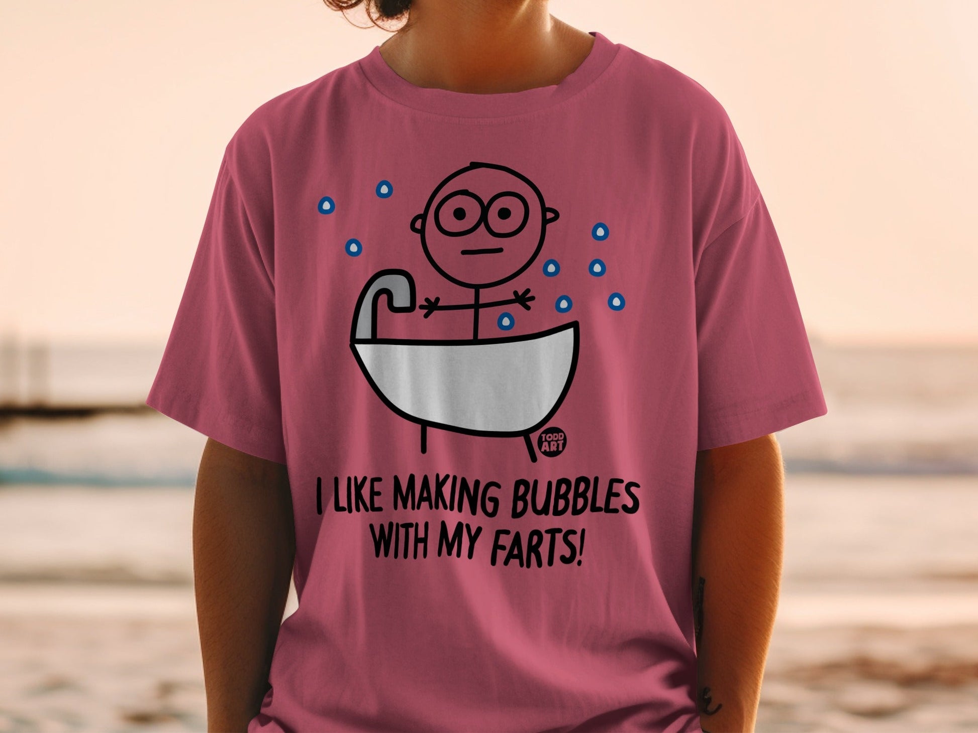 Pink t-shirt with cartoon man in bathtub, "I LIKE MAKING BUBBLES WITH MY FARTS!" text.