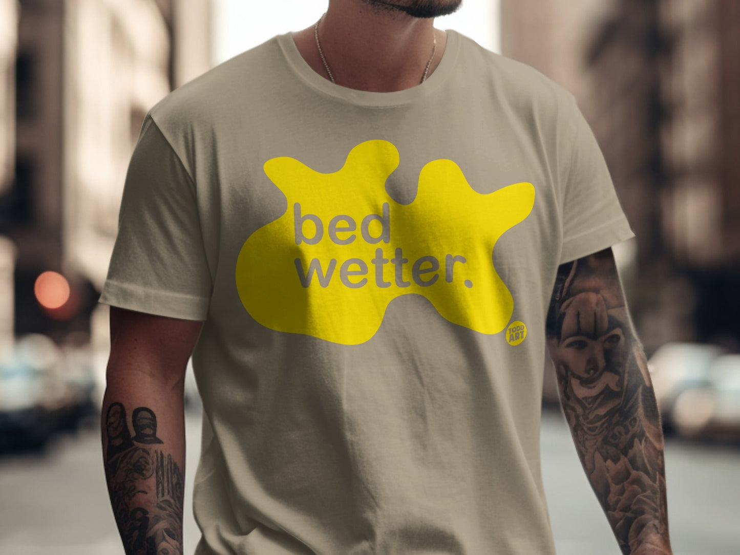Tan t-shirt with a yellow blob graphic and "bed wetter" text.