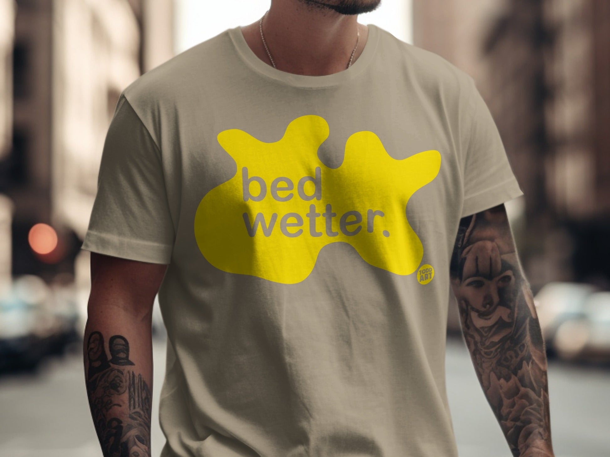 Tan t-shirt with a yellow blob graphic and "bed wetter" text.