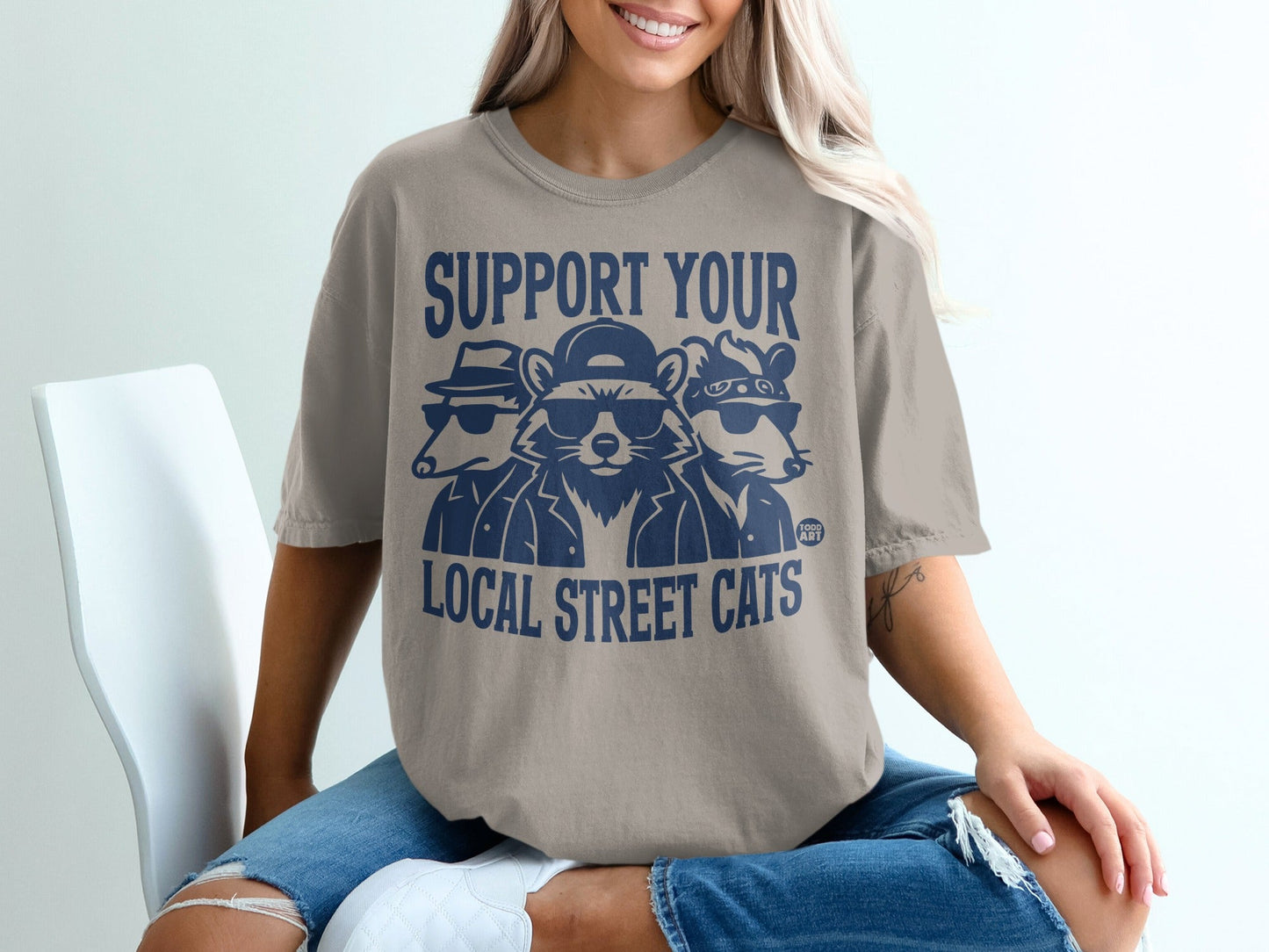 T-shirt with a graphic of three raccoons wearing sunglasses and hats.