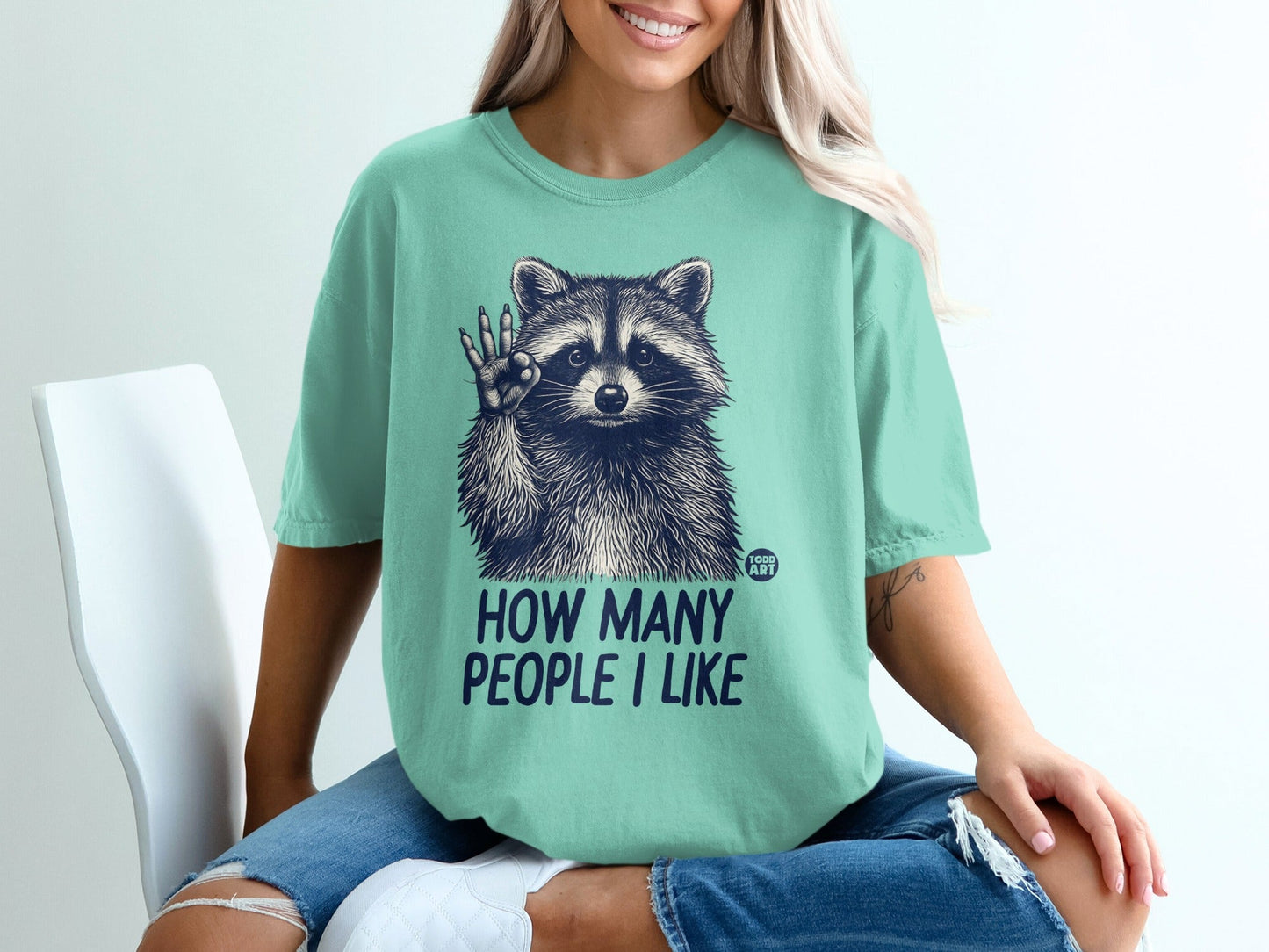 T-shirt with raccoon graphic and text "HOW MANY PEOPLE I LIKE".