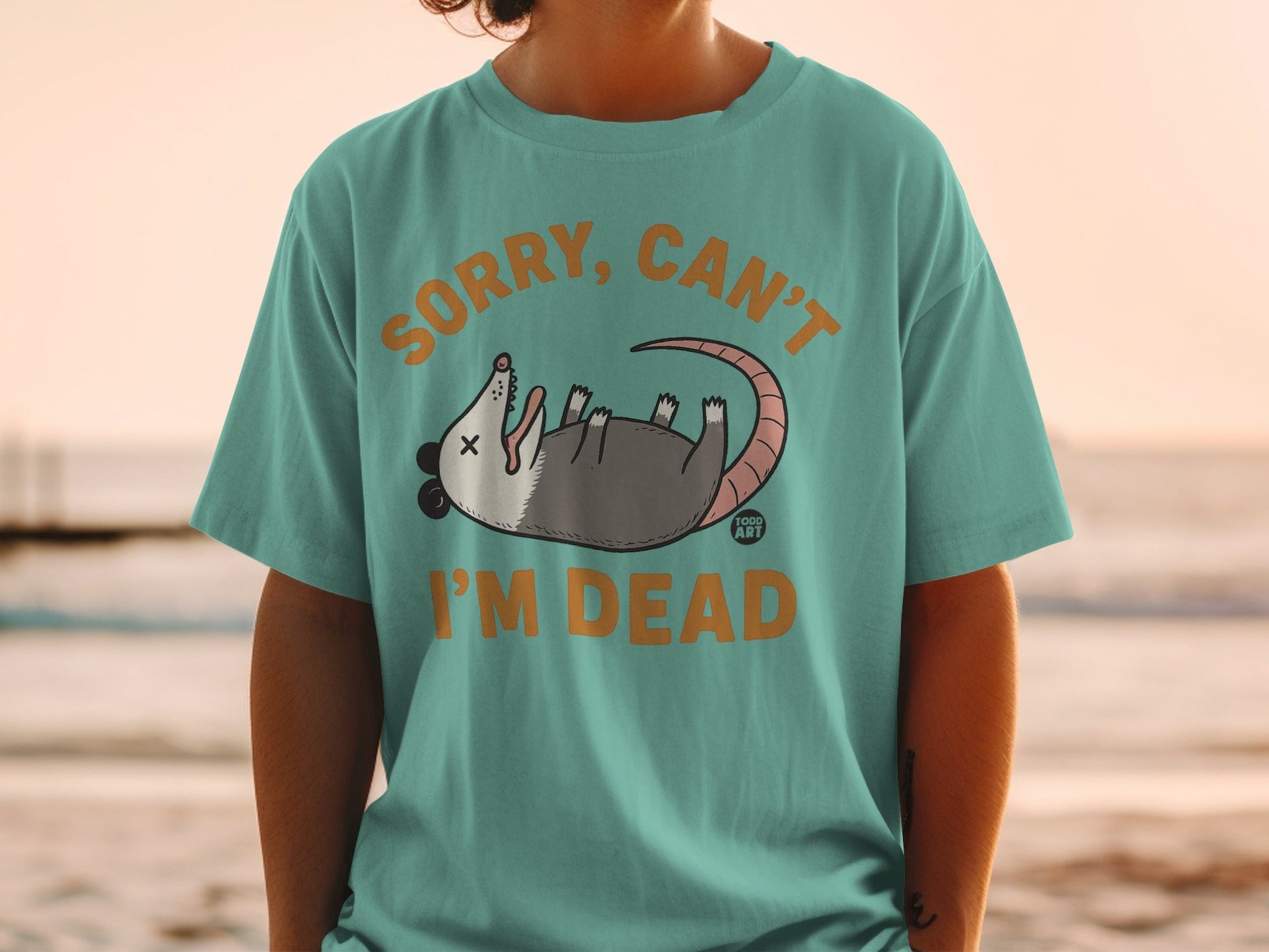Green t-shirt with cartoon opossum and text "Sorry, Can't I'm Dead."