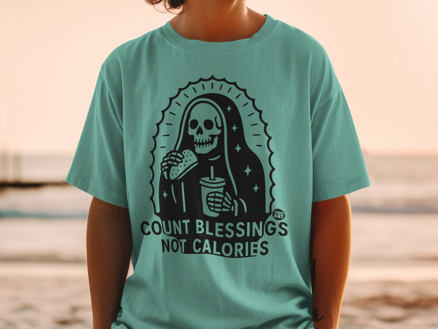 Teal t-shirt with grim reaper holding burger and drink, "COUNT BLESSINGS NOT CALORIES" text.