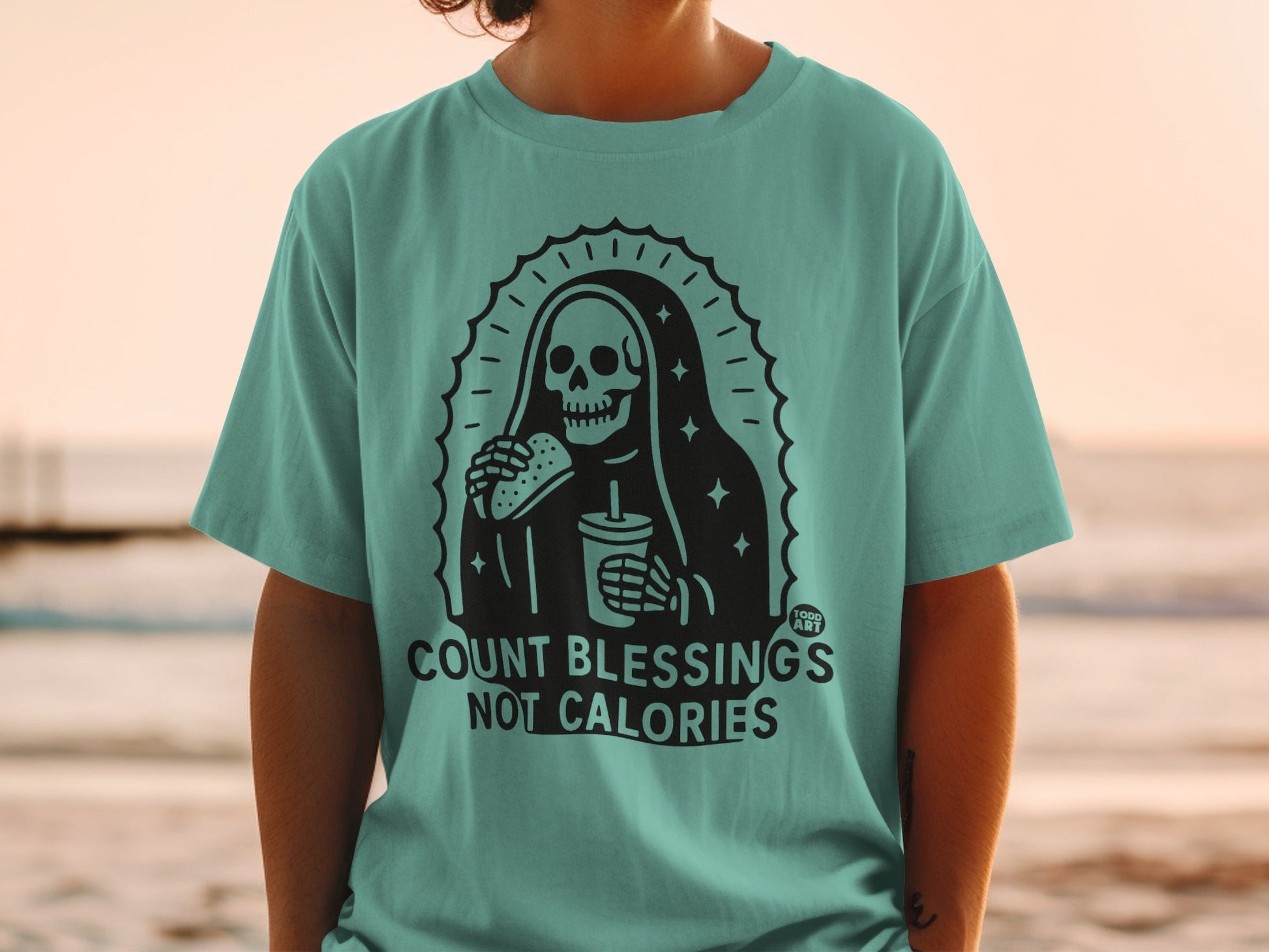 Teal t-shirt with grim reaper holding burger and drink, "COUNT BLESSINGS NOT CALORIES" text.
