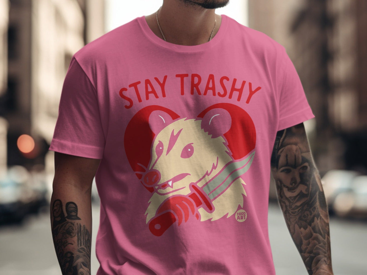 Pink t-shirt with "Stay Trashy" text and opossum with knife illustration.