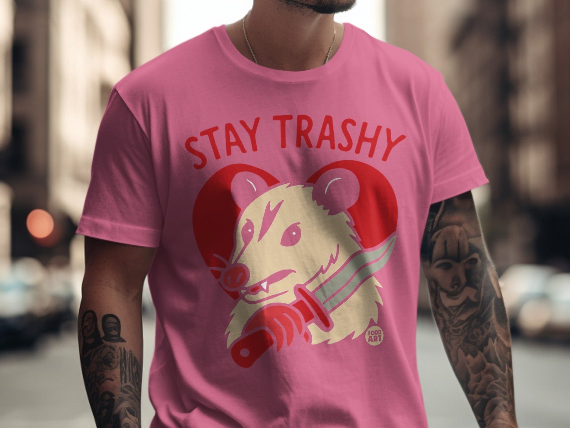 Pink t-shirt with "Stay Trashy" text and opossum with knife illustration.
