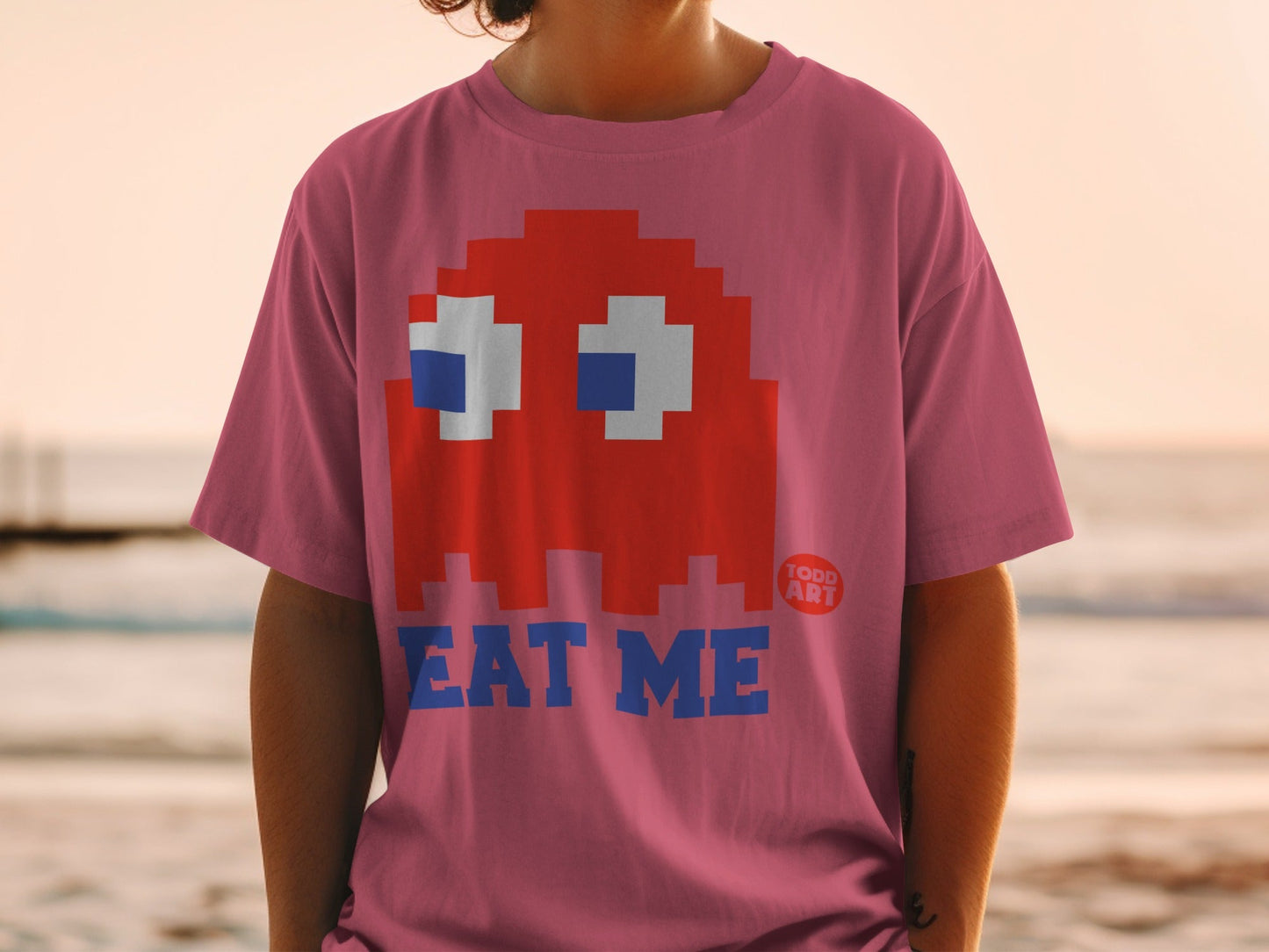 Pink t-shirt with red Pac-Man ghost and "EAT ME" text.