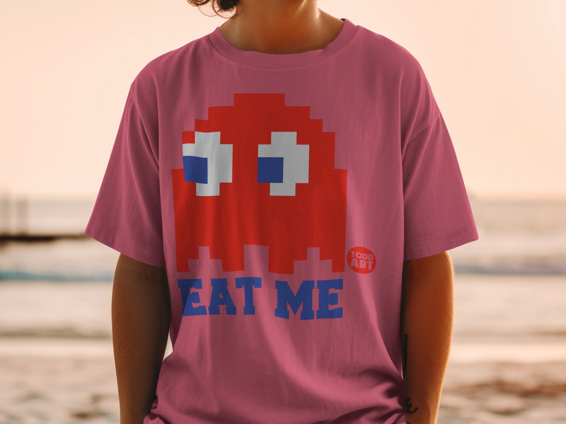 Pink t-shirt with red Pac-Man ghost and "EAT ME" text.