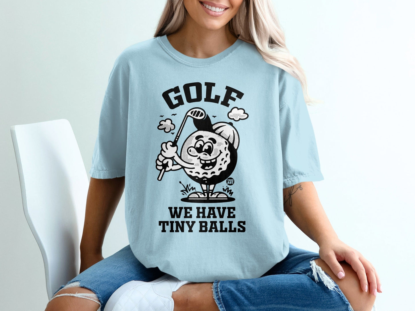 Light blue t-shirt with cartoon golf ball character and "WE HAVE TINY BALLS" text.