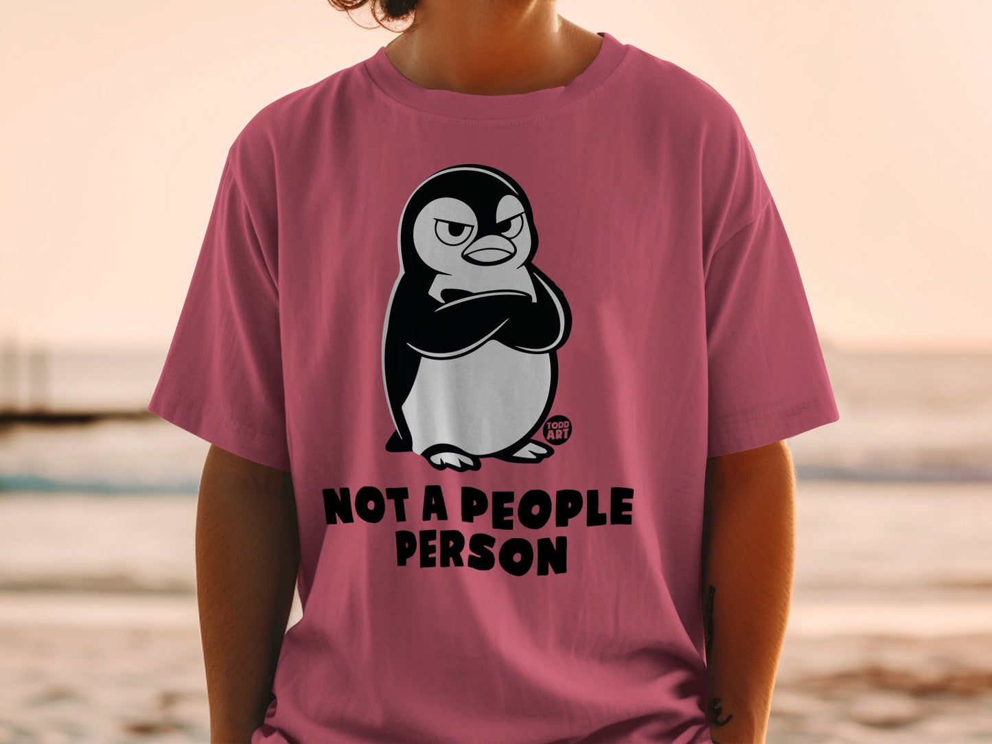 Pink t-shirt with grumpy penguin graphic and text "NOT A PEOPLE PERSON".