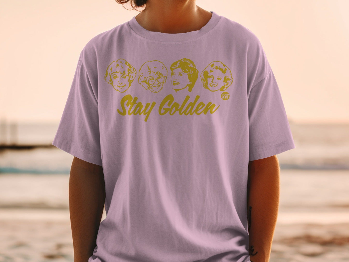 Lilac t-shirt with "Stay Golden" and The Golden Girls faces.