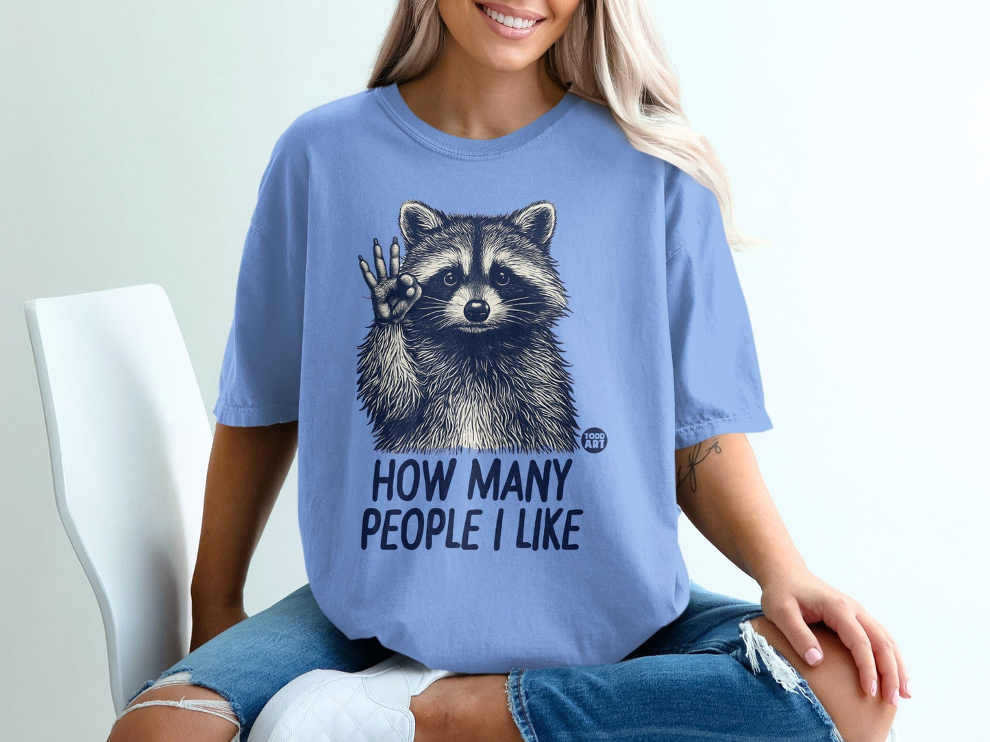 Blue t-shirt with raccoon graphic and "HOW MANY PEOPLE I LIKE" text.