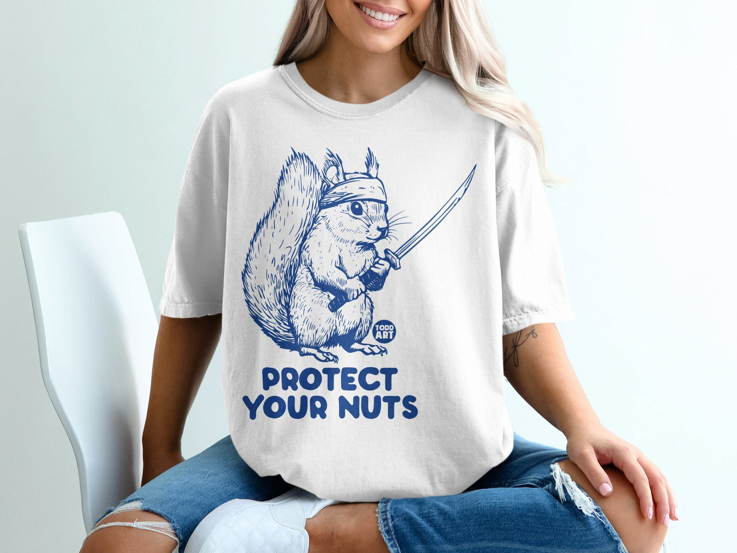 White t-shirt with blue graphic of a ninja squirrel holding a sword, text reads "PROTECT YOUR NUTS".