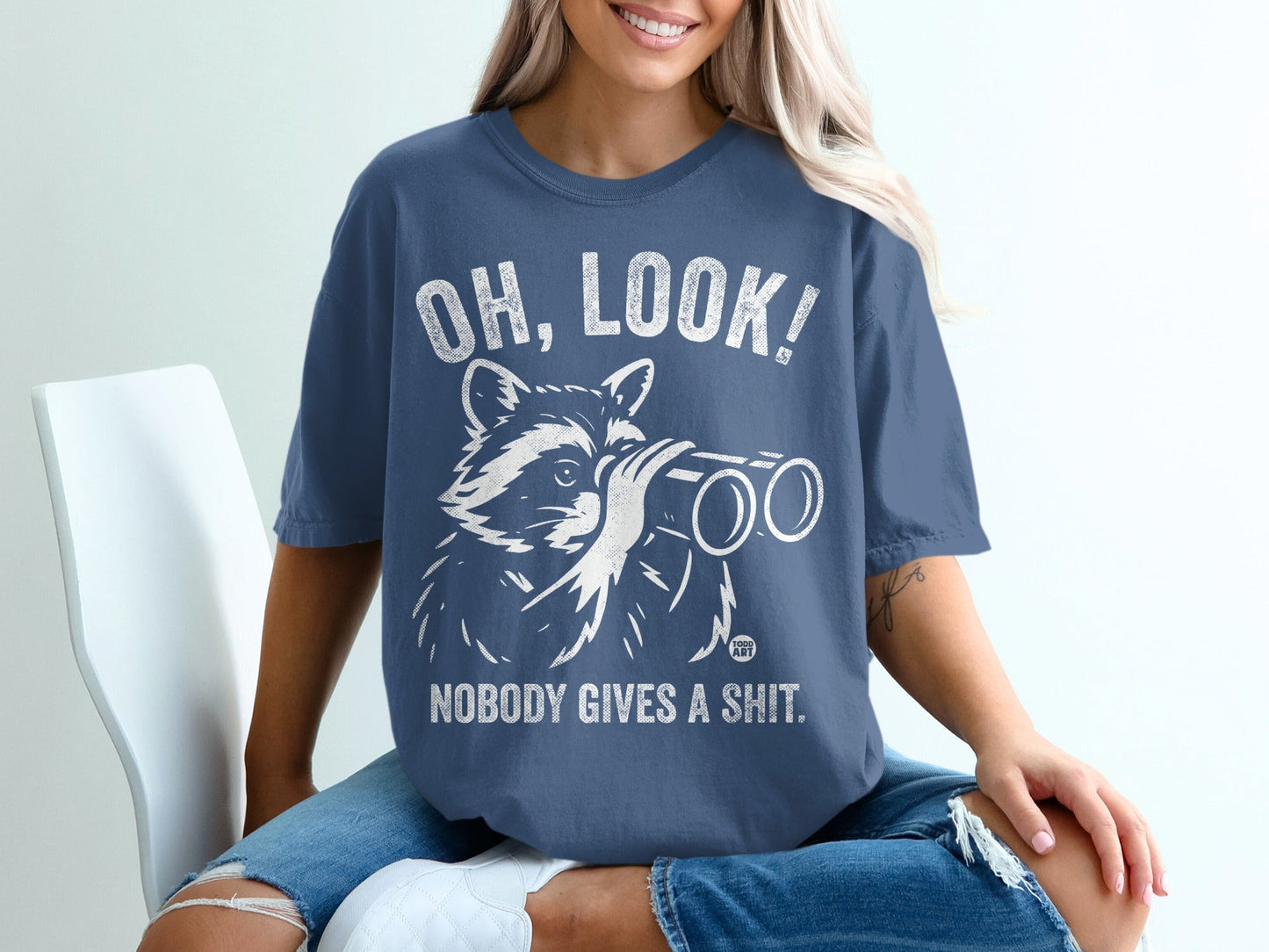 Blue t-shirt with raccoon holding binoculars and text "OH, LOOK! NOBODY GIVES A SHIT."